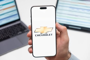 PRAG, CZECHIA - ŞUBAT 2024: Chevrolet otomobil logosu arka planda insan eli ve dizüstü bilgisayarında akıllı telefon ekranında 