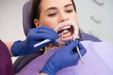Dişçi kliniğindeki genç bir kadının portresi. Lastik eldivenli dişçi kontrol yapıyor.