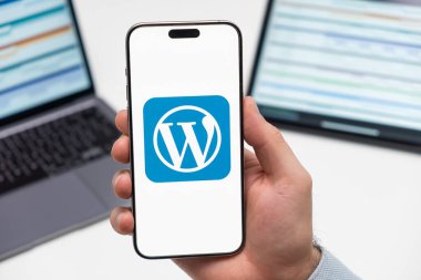 PRAG, CZECH REPUBLIC - 21 Ocak 2024: WordPress logosu, erkek elinin akıllı telefon ekranında, iş yerinde dizüstü bilgisayar ve tabletle birlikte.