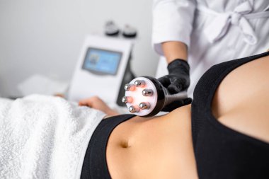 RF vücut boşluğu kaldırma prosedürü güzellik salonunda genç bir kadına göbek yağlarını azaltmada yardımcı olmak için kullanılır..