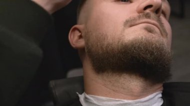 Berber, adam sakalını kesip berber dükkanında şık bir şekil veriyor. Kuaför erkek müşteriyle kuaförde makine kullanarak çalışıyor.