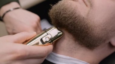 Kuaför, müşterinin boynundaki kılları traş eder. Berber dükkanında yakın plan makineyle sakal şekli yaratır. Berber kuaförde elektrikli tıraş makinesi kullanıyor.