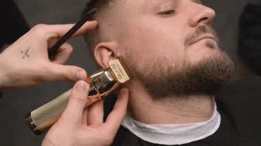 Stilist, berber dükkanında sakallı müşteriyle çalışırken budama ve tarak kullanıyor. Berber kuaförde saç kesiyor.