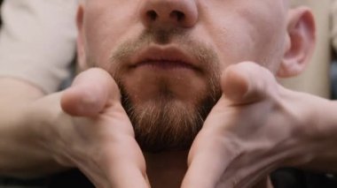 Berber, kuaförde sakal şekillendiriyor ve elleri okşuyor. Dikkatli kuaför, kuaförde erkek müşterinin yüz bakımını şekillendirir. Görünüm bakımı