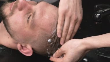 Berber, berber dükkanında köpüklü şampuan masajı yapan adamın kafasını lavaboya yapıştırıyor. Stilist, profesyonel saç bakımlı erkek müşteriye hizmet veriyor