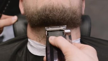 Master, berber dükkanında müşteri sakalını otomatik budayıcıyla kesiyor. Kuaför kuaförde modern ekipmanlarla saç kesimi yapıyor.