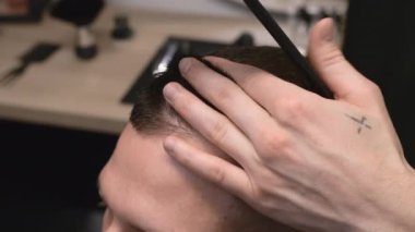 Berber, berber dükkanında adamın ıslak saçlarını makas ve tarak ile kesmesini sağlıyor. Aletleri olan kuaför, müşteriyle kuaförde çalışır.