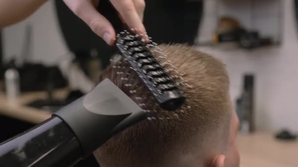 バーバーは床屋のクローズアップで乾燥機で吹く男の髪をブラシをかけます プロのヘアスタイリストは グルーミングサロンでヘアスタイルのためのツールを使用しています — ストック動画