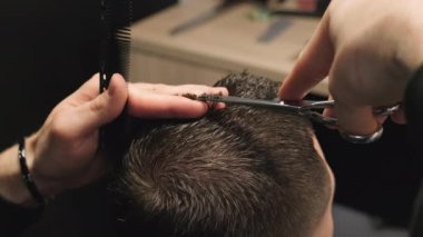 Berber, berber dükkanında adamın saçını parmaklarıyla kesiyor. Kuaför kuafördeki beyefendinin saçını kesmek için keskin makas kullanıyor.