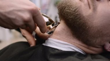 Kuaför, berber dükkanında müşterinin sakalını kesmek için budama makinesi kullanıyor. Yetenekli berber, erkeklerin güzellik salonundaki aletlerle yüz kesimi yapıyor.