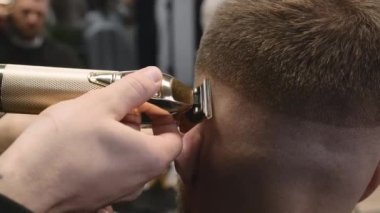 Kuaför, modern berber dükkanında müşteri saçını elektrikli budayıcıyla tıraş ediyor. Berber güzellik salonunda zarif bir saç kesimi yapıyor.