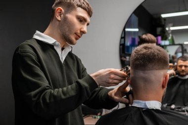 Genç berber, berber dükkanında adamın saçını ustalıkla kesiyor.