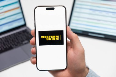 PRAGUE, CZECH REPUBLIC - 21 HAZİRAN 2024: İş arka planında erkek elinin akıllı telefon ekranında Western Union logosu. 