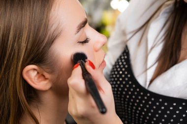 Makyaj sanatçısı, güzellik salonunda özel bir fırçayla müşterilerin yüzüne hafifçe vurgu yapar.