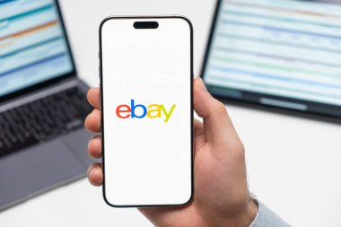 PRAG, CZECH REPUBLIC - 21 HAZİRAN 2024: eBAy logosu iş arka planında çalışan erkeklerin elinde akıllı telefon ekranında. 