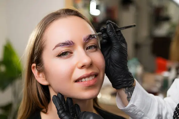 stock image Eyebrow artist applies foam to cleanse before procedure. Woman worker in latex gloves prepares client skin for enhancement process