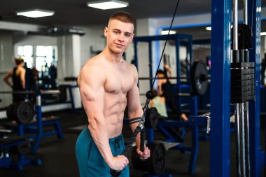 Spor salonunda trisepsleri kablo makinesiyle çalıştıran bir adamın portresi.. 