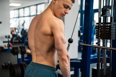 Genç profesyonel bir vücut geliştirici, trisepslerini spor salonunda bir kablo makinesiyle eğitiyor.