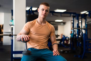 Vücut geliştirici spor salonunda bir dambıl tutar ve egzersiz yapmaya ara verir.