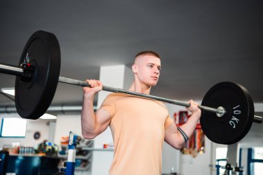 Sarışın genç adam vücut geliştirici spor salonunda ağırlık çalışıyor.