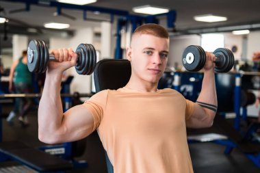 Vücut geliştirici, spor salonunda dambılları kaldırarak omuzlarını eğitir.