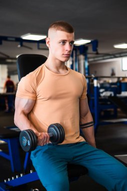 Genç bir vücut geliştirme ustasının portresi bir halterle biseps kıvrımı yapıyor.