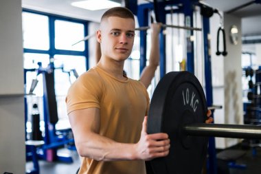 Genç vücut geliştiricinin portresi spor salonunda ağır bir plaka taşıyor.