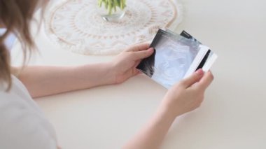 Genç kadın, masada oturan gelecekteki bebek ultrason muayenesinin resimlerine bakıyor. Neşeli hamile kadın düzenli doğum öncesi kontrolünden geçiyor.