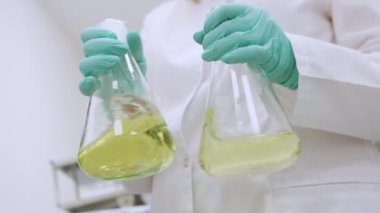 Laboratuvar önlüğü giymiş kimyager ve lastik eldivenler analizden önce sarı örnekleri titizlikle sallıyor.