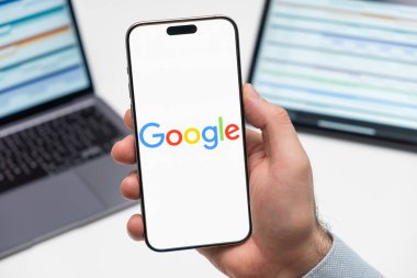 PRAG, CZECHIA - Temmuz 2024: Google logosu arka planda erkek eli ve dizüstü bilgisayarda akıllı telefon ekranında 