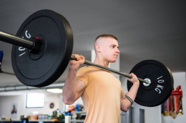 Genç sarışın vücut geliştirici spor salonunda halter kaldırıyor.