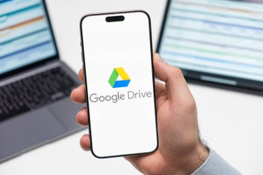 PRAG, CZECHIA - JULY, 2024: Google Drive logosu arka planda erkek eli ve dizüstü bilgisayarda akıllı telefon ekranında 