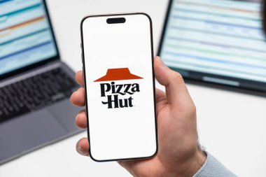 PRAG, CZECHIA - Temmuz 2024: Pizza Hut logosu arka planda erkek eli ve dizüstü bilgisayarda akıllı telefon ekranında 