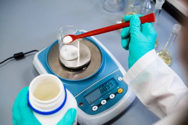 Bir kadın kimyager, toz örneklerini laboratuvar dengeleriyle ölçer.