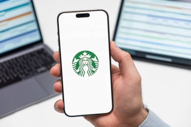 PRAG, CZECHIA - Temmuz 2024: Starbucks logosu arka planda erkek eli ve dizüstü bilgisayarında akıllı telefon ekranında 