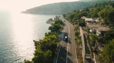 Çatı üzerinde kürek tahtası olan otomobil, sahil yolu boyunca döner gider. Gök mavisi deniz suyunun büyüleyici manzarası ve gün batımında yamaçta küçük bir köy.