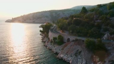 Minivan, alacakaranlıkta otoyol boyunca turist minibüsünü takip ediyor. Kıyı şeridine yakın yamaçtan esen rüzgarlar dağlar ve ormanlar tarafından çerçeveleniyor.