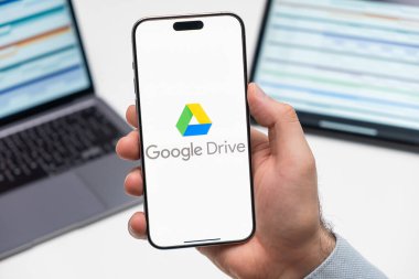 PRAG, CZECHIA - JULY, 2024: Google Drive logosu arka planda erkek eli ve dizüstü bilgisayarda akıllı telefon ekranında 