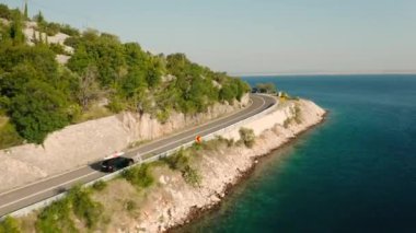 Çatıya monte edilmiş kürek tahtası olan araba yol boyunca gider. Dönek otoyol tepenin eteklerine kadar uzanıyor. Denize karşı ormanlar ve turkuaz su.