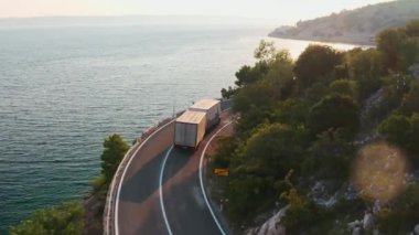 Kargo kamyonu konteynırla gün batımında dağlık yolda ilerliyor. Deniz manzarası yakınındaki dağ yüksekliğinde seyehat.