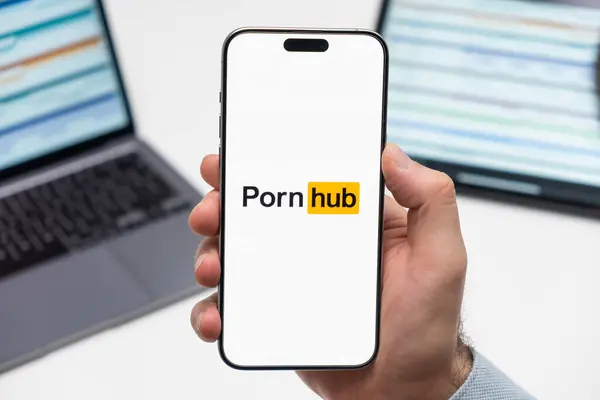 stock image PRAGUE, CZECHIA - JULY, 2024: Porn hub logo on the screen of smartphone in mans hand and laptop on the background 