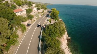 Çatıda kürek tahtası olan araba sahil yolu boyunca gider. Otoyol yeşil ve turkuaz deniz suyuyla muhteşem tepe manzarası açıyor.