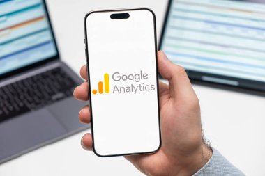 PRAG, CZECHIA - JULY, 2024: Google Analitik logosu arka planda erkek eli ve dizüstü bilgisayarda akıllı telefon ekranında 