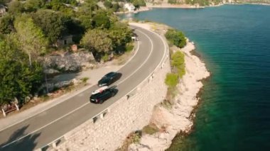 Çatıda SUP tahtası olan bir turist arabası göl kenarındaki göl suyuyla yol boyunca gider. Araç, yaz günü dolambaçlı sahil yolunda yol alır.