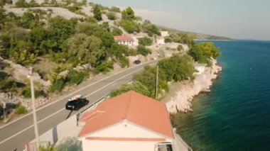 Çatıda SUP panosu olan araba sahil yolu boyunca gidiyor. Taze esintili gök mavisi yaz tatili boyunca neşeli bir hava yaratır.