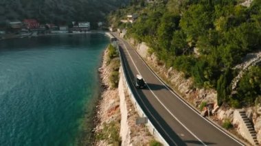 Dar bir sahil boyunca kürek çeken siyah bir araba berrak mavi bir gökyüzünün altında temiz bir su ve bir yol..