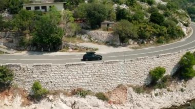 Çatı kutulu otomobil göl kıyısından göl kenarındaki göl suyuna gidiyor. Deniz ve kayalık yamaç arasındaki otoyol büyüleyici manzaralar yaratır.