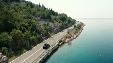 Çatı kutulu araba yaz günü kayalık yamaçlı sahil yolu boyunca gider. Macera gök mavisi deniz ve manzara manzarası sunar.