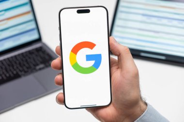 PRAG, CZECHIA - Temmuz 2024: Google logosu arka planda erkek eli ve dizüstü bilgisayarda akıllı telefon ekranında 