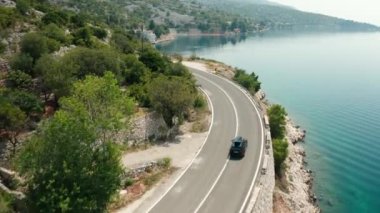 Çatı kutusu olan siyah araba, parlak bir yaz gününde dolambaçlı bir sahil yolunda ilerliyor.